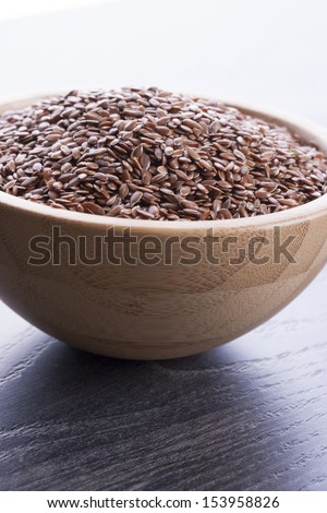 Close up photo of a raw eco food in the wooden bowl - dark brown linseeds placed on a dark wooden background.
