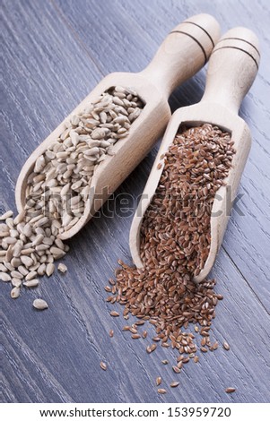 Close up photo of a raw eco food in the wooden spatula - light brown sunflower seeds and dark brown linseeds placed on a dark wooden background.