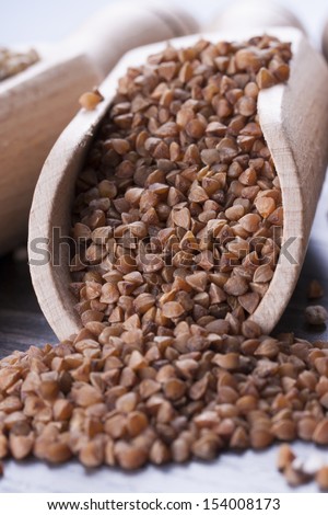 Close up photo of a raw eco food in the wooden spatula - dark brown kasha placed on a dark wooden background.