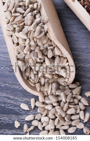 Close up photo of a raw eco food in the wooden spatula - light brown sunflower seeds placed on a dark wooden background.