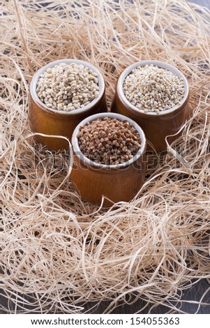 Close up photo of a raw eco food in the clay cup - light brown buckwheat groats, dark brown kasha and brown pearl barley placed on a dark wooden background.