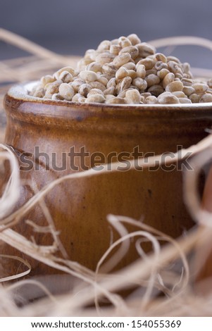 Close up photo of a raw eco food in the clay cup - brown pearl barley placed on a dark wooden background.