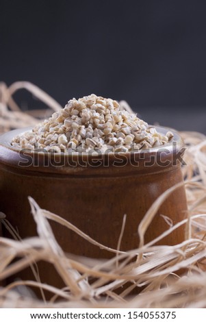 Close up photo of a raw eco food in the clay cup - light brown buckwheat groats placed on a dark wooden background.