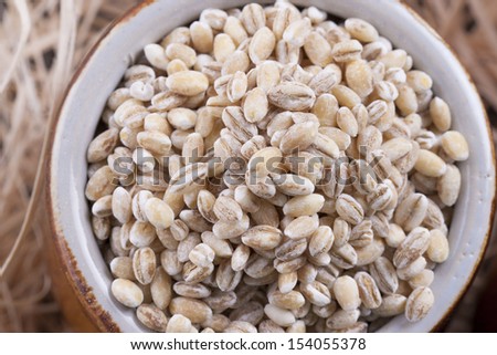Close up photo of a raw eco food in the clay cup - brown pearl barley placed on a dark wooden background.