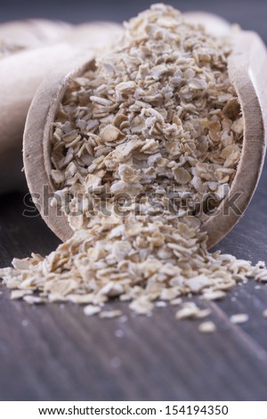 Close up photo of a cereal grain product in a wooden scoop - mid-brown arena bran placed on a dark wooden background.