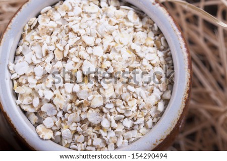 Close up photo of a cereal grain product in a clay cup - light brown barley flakes placed on a wooden shavings.