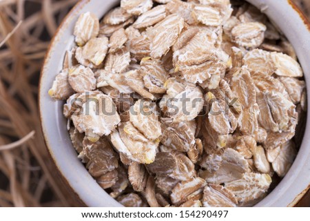 Close up photo of a cereal grain product in a clay cup - dark brown secale flakes placed on a wooden shavings.