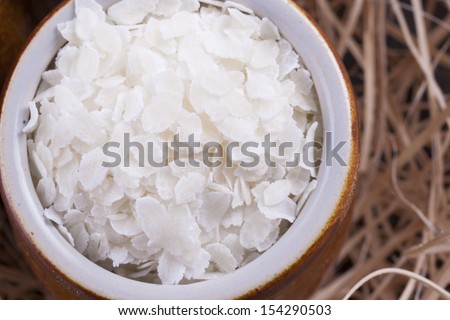 Close up photo of a cereal grain product in a clay cup - white rice flakes placed on a wooden shavings.