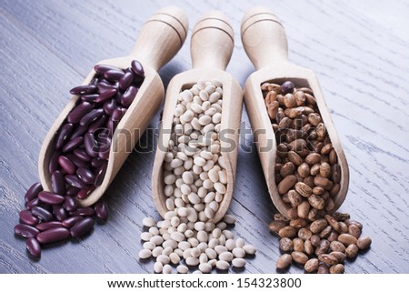 Close up photo of a beans in wooden scoop - brown pinto beans, red beans and white beans placed on a dark wooden background.