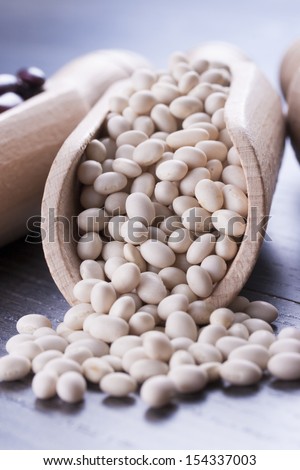 Close up photo of a beans in wooden scoop - white beans placed on a dark wooden background.