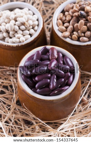 Close up photo of a beans in clay cup - brown pinto beans, red beans and white beans placed on a wooden shavings.