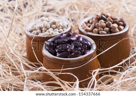 Close up photo of a beans in clay cup - brown pinto beans, red beans and white beans placed on a wooden shavings.
