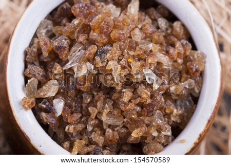 Close up photo of a food ingredients in a clay cup - large pieces of crystalized sugar placed on a wooden shavings.