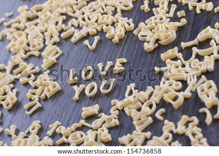 Close up photo of a letter noodles - Love you text placed on a dark wooden background.