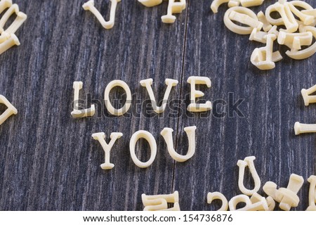 Close up photo of a letter noodles - Love you text placed on a dark wooden background.