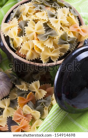 Raw food composition - yellow, green and orange colored farfelle pasta placed on a bright background.