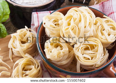 Raw food composition - yellow tagliatelle in a clay pot on a bright background.
