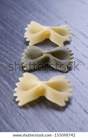 Raw food composition - yellow and green farfalle pasta on a dark wooden background.