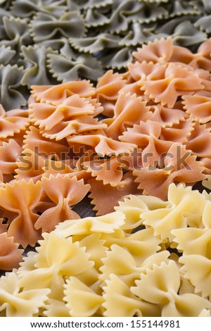 Raw food composition - yellow, orange and green farfalle pasta close up photo.