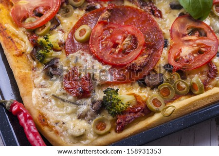 Close up of the just baked homemade pizza with tomato, salami slices and olives placed on a black tray.