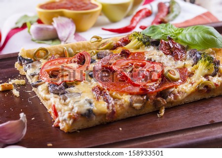 Close up of the just baked homemade pizza with tomato, salami slices and olives placed on brown cutting board.