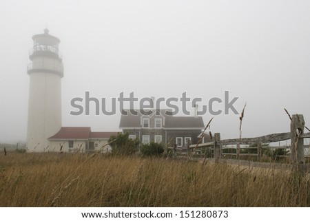 A lighthouse in the fog with a field in front.  Highland Light, Cape Cod National Seashore, MA, USA.