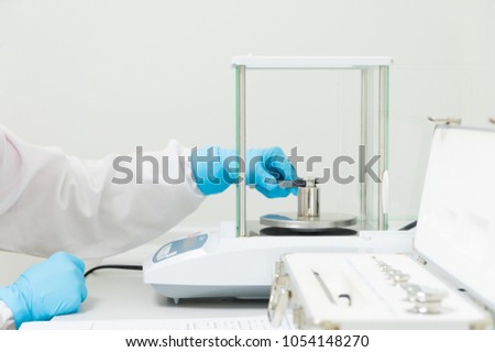 The operator\'s hand is holding stainless steel calibration weight to place on the analytical balance pan for the calibration test, concept of quality control laboratory in pharmaceutical industry.