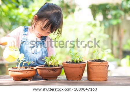 Adorable 3 years old asian little girl is watering the plant  in the pots outside the house, concept of plant growing learning activity for preschool kid.
