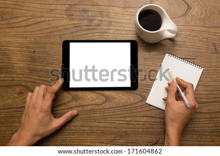 Close-up of male hands using a digital tablet and writing notes with a cup of coffee
