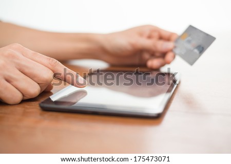 Close up of a person typing on a digital tablet device and holding a credit card while shopping online