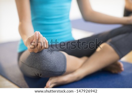Low section of mid adult woman practicing yoga while sitting on exercise mat at gym