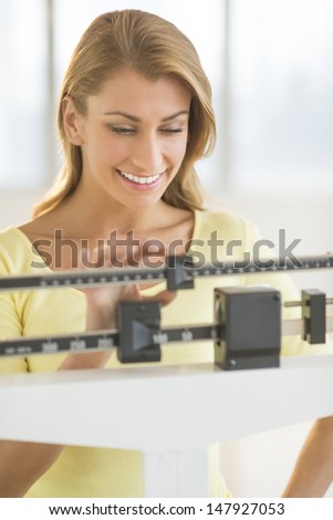Happy young Caucasian woman weighing herself on balance scale at health club