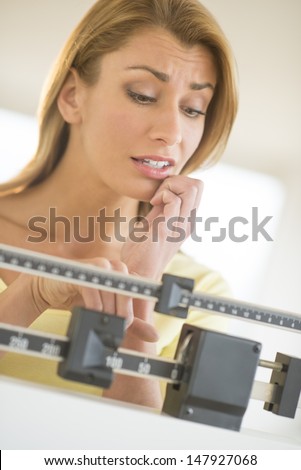 Worried young Caucasian woman using balance weight scale at health club