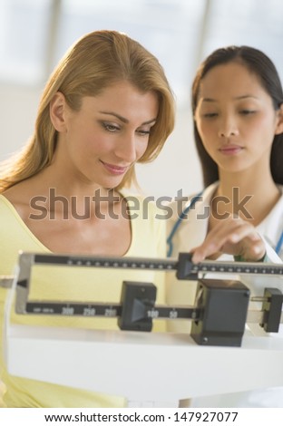 Mid adult female doctor weighing woman on balance weight scale in clinic