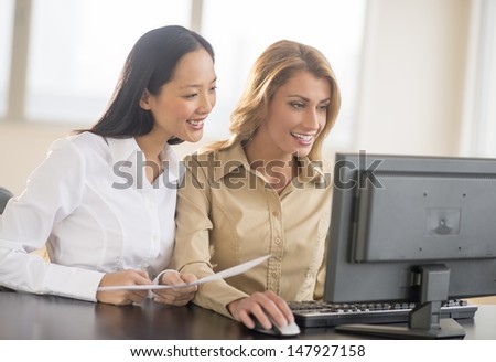 Happy multi-ethnic businesswomen using computer together at desk in office