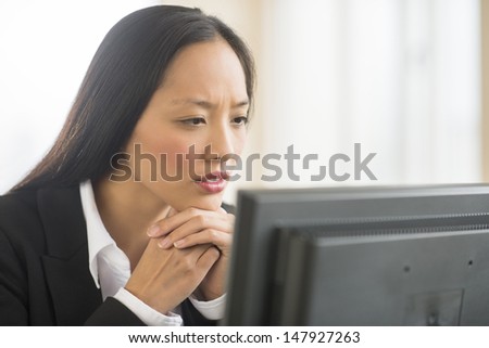 Close-up of mid adult businesswoman with hand on chin looking at computer in office