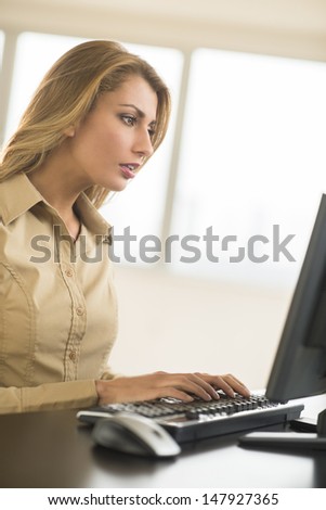 Young Caucasian businesswoman using Desktop PC at desk in office