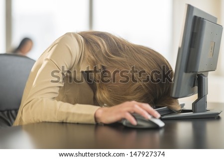Tired young businesswoman with head on computer keyboard at desk in office