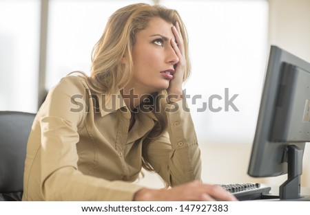 Frustrated young businesswoman looking up while sitting at computer desk