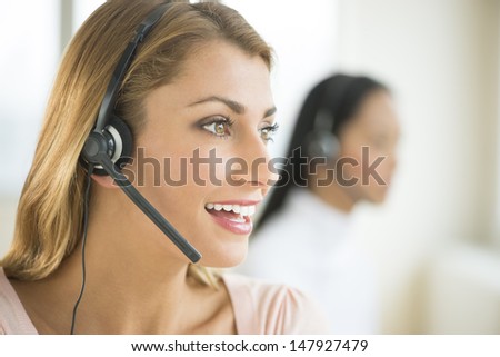Happy female customer service representative looking away with colleague in background