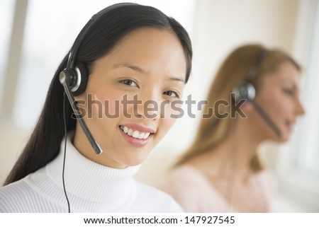 Portrait of female customer service representative smiling at office with colleague working in background