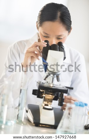 Mid adult Asian female scientist using microscope at desk in laboratory