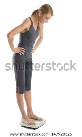 Full length of happy young woman with hands on hips using weight scale isolated over white background