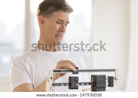 Worried mature man using balance weight scale at gym