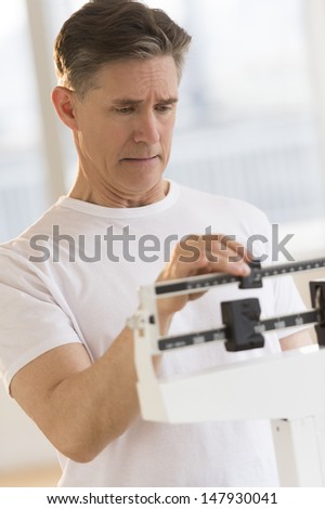 Worried mature man checking his weight on balance scale at health club