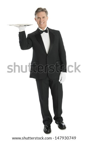 Full length portrait of confident mature waiter carrying tray while standing isolated over white background