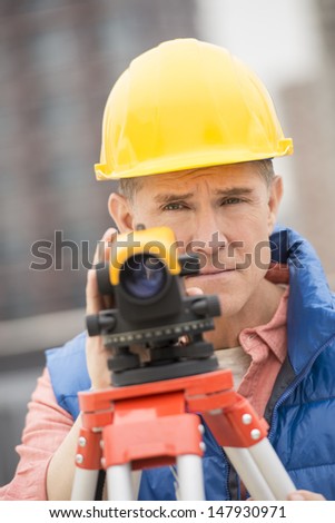 Portrait of confident mature construction worker with theodolite standing at construction site