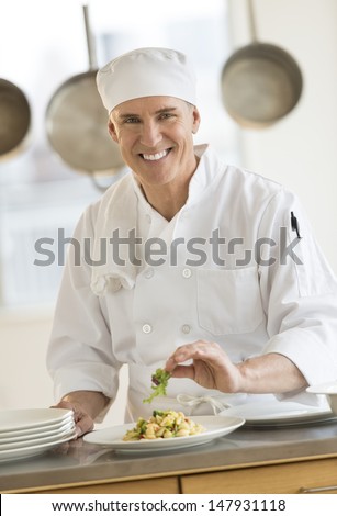 Portrait of happy male chef garnishing pasta dish in commercial kitchen
