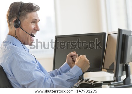 Side view of excited mature male trader screaming while using multiple computers at desk in office