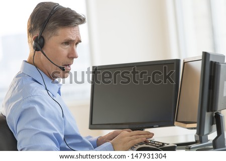 Side view of male trader using multiple computer screens while communicating through headphones at desk